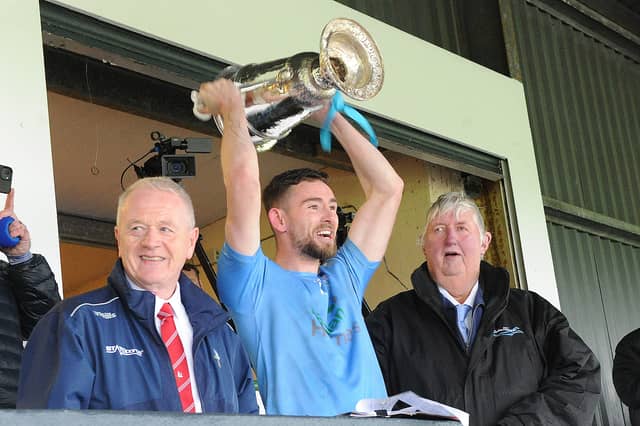 Newtown Blues captain, Ciarán Downey, lifts the Joe Ward Cup, with Seán McClean (LCB chairman) (left) Seamus Keenan (sponsor Anchor Tours)