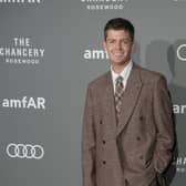 Jamie Miller smiling while posing for photos at a red carpet event, wearing a brown suit