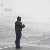 A man looks at a flooded road amid blustery weather